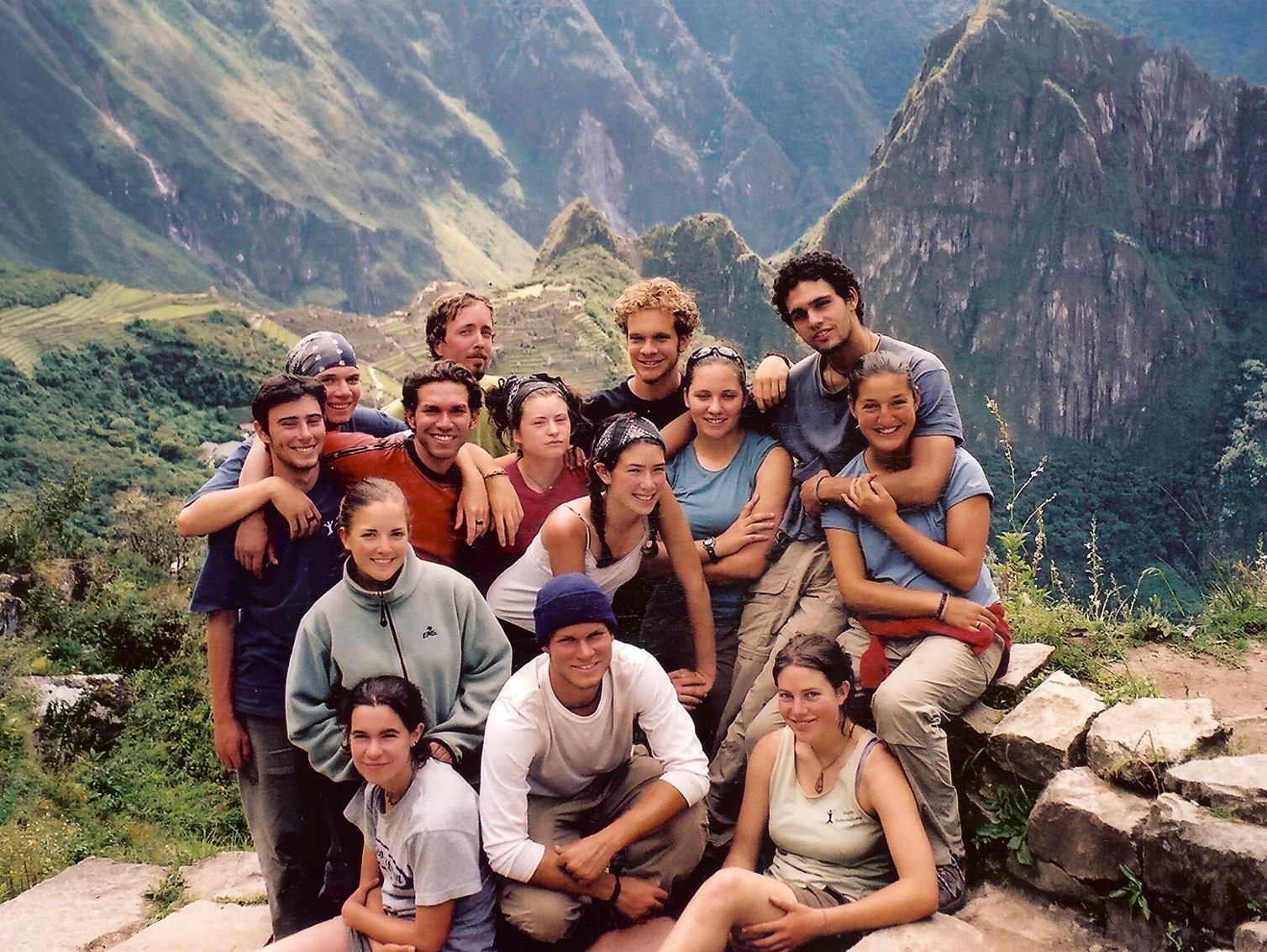 A group of fourteen men and women posing in front of a mountainous landscape